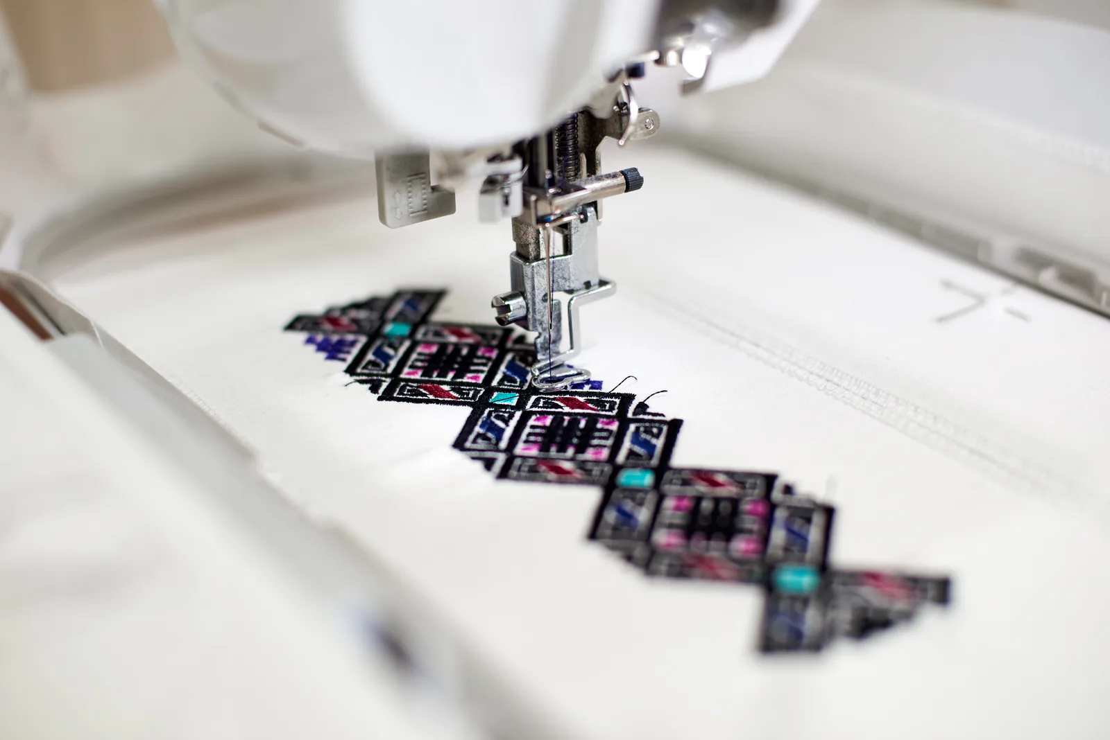 Embroidery machine stitching a geometric pattern on white fabric