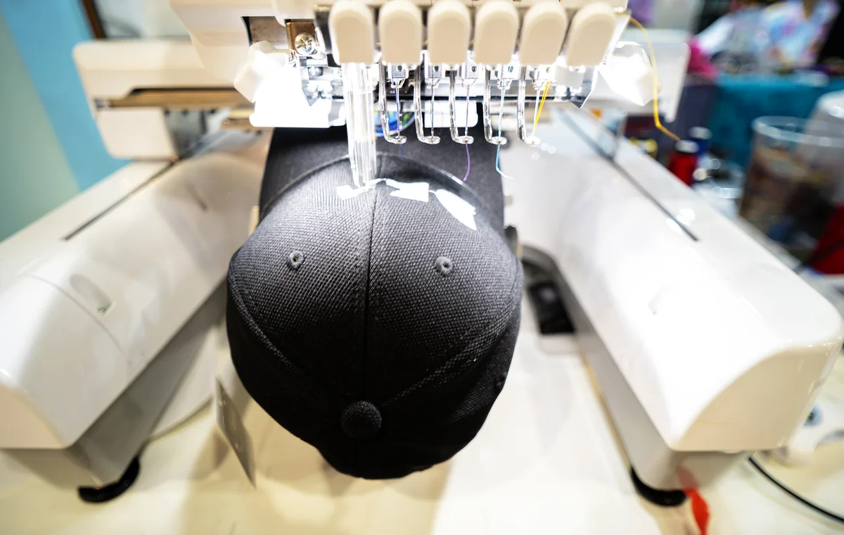 Computerized embroidery machine stitching a logo onto a black cap